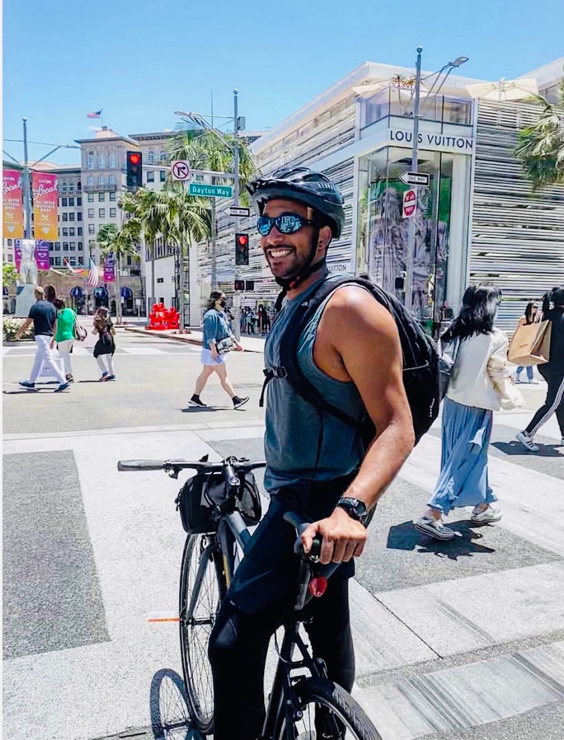 a photo of a man wearing a helmet and sunglasses next to a bicycle outside in beverly hills, ca