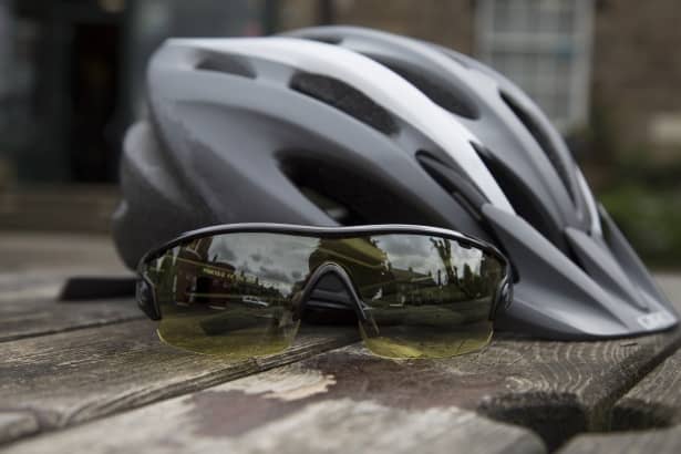 a pair of sunglasses next to a grey and white bike helmet on a wooden table