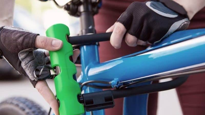 a close up of a person closing a green and black lock on a bright blue bicycle. the person is wearing black fingerless gloves.